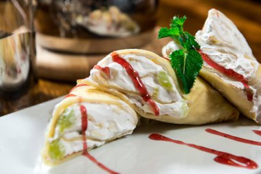 Tatlı. Kremalı ve meyveli krep. Ahşap bir masaya şerbet ve nane ile süslenmiş.