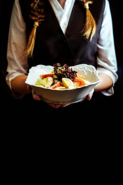 Garsonun ellerinde taze sebze salatası var.