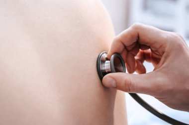 Doktorun eli adamın sırtında bir fonendoskop tutuyor. Hastane ofisinde bir hastanın sağlık kontrolü.