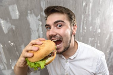 Ağzını açıp hamburger yiyen genç bir adamın portresi.
