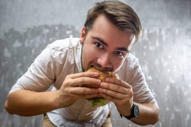 Ağzını açıp hamburger yiyen genç bir adamın portresi.