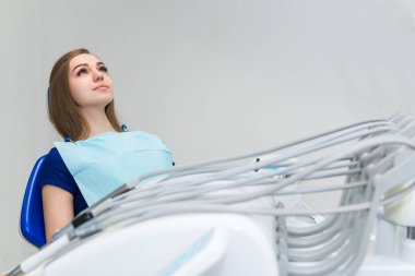 Klinikte dişçi koltuğunda doktor bekleyen genç bir hasta.