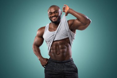 Stüdyoda poz veren Afrikalı Amerikalı bir sporcu. Gömleğin altındaki karın kaslarını gösteriyor.
