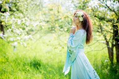 Güzel kız bahar elma bahçesinde duruyor uzun bir elbiseyle