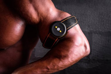 Afrika kökenli Amerikalı erkek vücut geliştirici siyah arka plan üzerinde bisepsi eğitmek için elektronik miostimülatör kullanıyor.