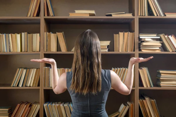 Студентка выбирает книгу из книжного шкафа в библиотеке — стоковое фото