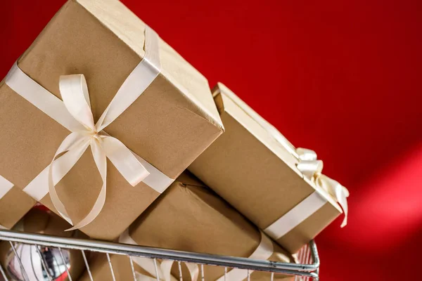 Geschenke in Bastelpapier mit weißem Klebeband im Einkaufswagen auf rotem Hintergrund — Stockfoto