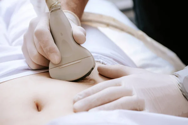 Ultrazvukový scanner v ruce profesionálního lékaře vyšetřujícího svého pacienta, který provádí ultrazvuk břicha skenující časné těhotenství pro mladou dívku — Stock fotografie