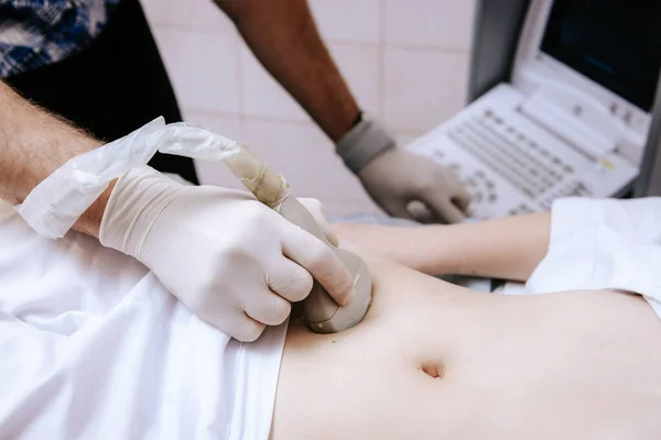 Ultrazvukový scanner v ruce profesionálního lékaře vyšetřujícího svého pacienta, který provádí ultrazvuk břicha skenující časné těhotenství pro mladou dívku — Stock fotografie
