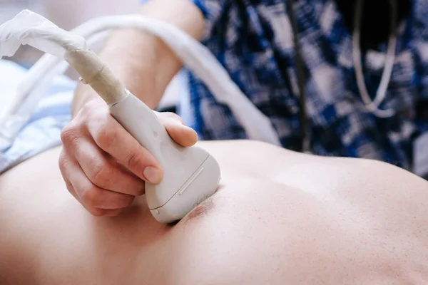 De dokter houdt een ultrageluid machine op zijn borst. Het hart van een patiënt controleren in een ziekenhuiskantoor — Stockfoto