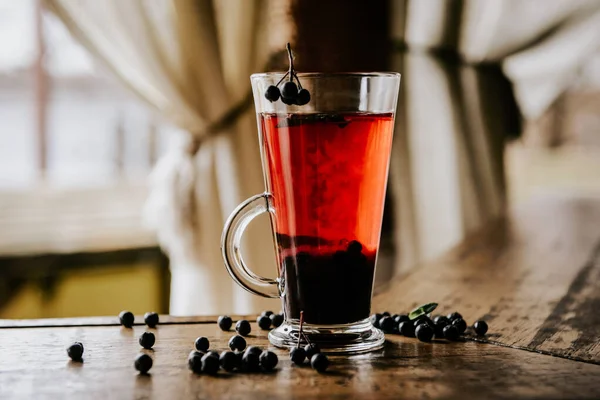 Чай с черной смородиной на деревянном столе в кафе. Горячий напиток в стакане — стоковое фото