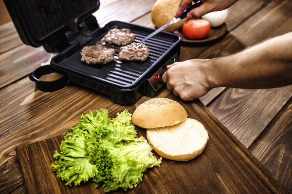 Cocinar hamburguesas caseras con parrilla eléctrica en una mesa de madera —  Fotos de Stock