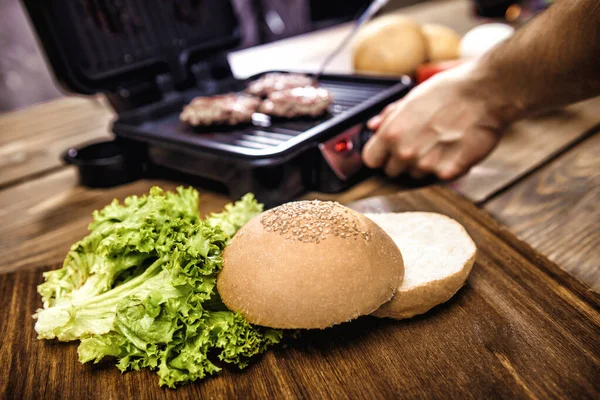 Готовить домашние гамбургеры с помощью электрического гриля на деревянном столе — стоковое фото
