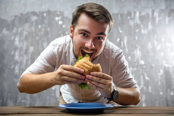 Портрет молодого человека, кусающего гамбургер с открытым ртом — стоковое фото