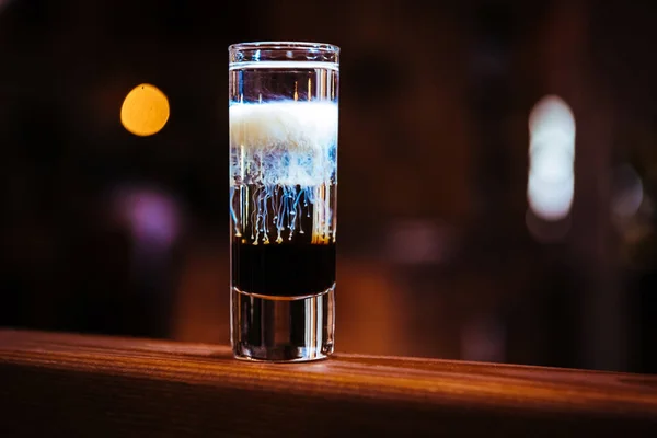 Short drink cocktail in layers with different types of alcohol on a wooden bar counter in a restaurant