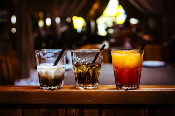 Différents cocktails alcoolisés avec glace dans un bar sur une table en bois — Photo