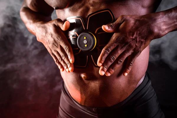 Bodybuilder αρσενικό Αφρικής χρησιμοποιεί ηλεκτρονική ζώνη μυϊκό διεγέρτη εκπαιδευτή για την τόνωση των κοιλιακών μυών — Φωτογραφία Αρχείου