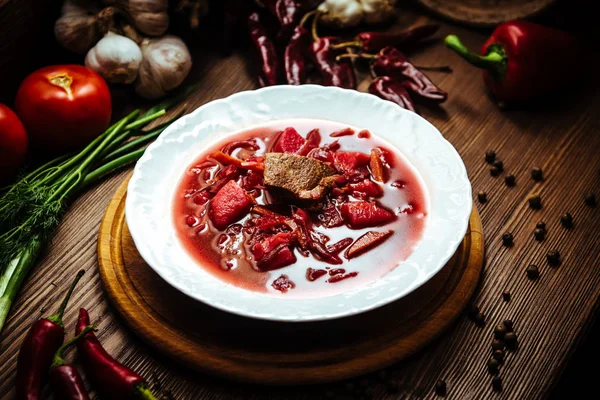 Vörös leves nevű borsch húsdarabokkal és fűszerekkel. Top view fából készült háttér együtt friss paradicsom, bors, hagyma és gyógynövények — Stock Fotó