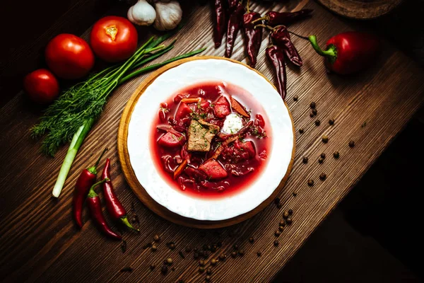 Vörös leves nevű borsch húsdarabokkal és fűszerekkel. Top view fából készült háttér együtt friss paradicsom, bors, hagyma és gyógynövények — Stock Fotó