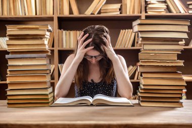 Genç kız öğrenci kütüphanede bir sürü kitapla bir masada oturan bir ders kitabı okur.