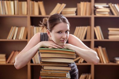 Genç kız kütüphanede bir yığın kitaba yaslandı.