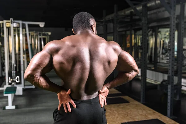 Fisiculturista afro-americano demonstra volumes impressionantes de músculos das costas no ginásio — Fotografia de Stock