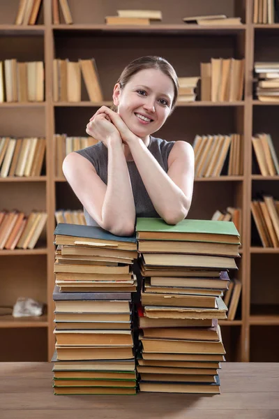 Una joven estudiante se apoyó en una pila de libros en la biblioteca — Foto de Stock