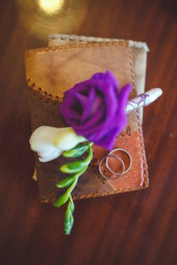 Yeni evlilerin düğün gününün ayrıntıları. Gelin ve damadın yüzükleri yaka çiçekleri ve pasaportlarla birlikte masanın üzerinde duruyor..