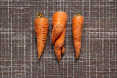 Kahverengi bir hasır arka planda normal sebzeler arasında deforme olmuş çirkin bir havuç, sıfır gıda atığı konsepti, üst görünüm