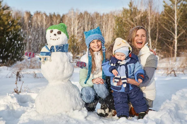 雪だるまを連れた陽気な家族の肖像画です冬の屋外で幸せな母親と子供たち. — ストック写真