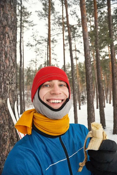 Portret van een mannelijke skiër die een banaan eet in een dennenbos. — Stockfoto