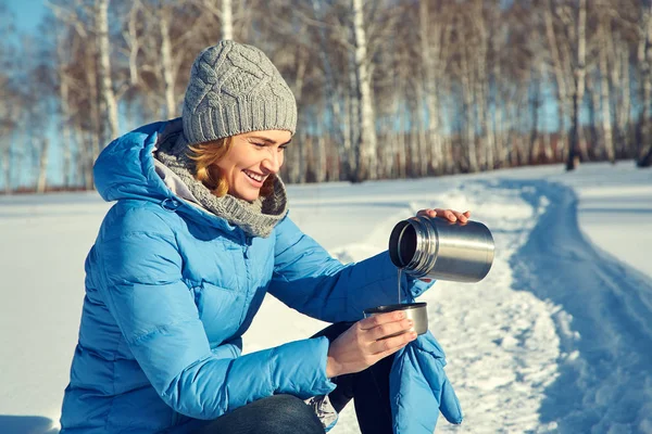 Vrouw op een wandeling in de winter bos drinken thee uit een thermoskan. — Stockfoto