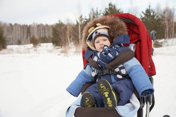Baby jongen zittend in een kinderwagen in de winter buiten. — Stockfoto