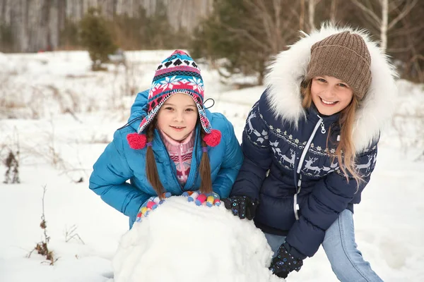 Две подруги строят снеговика. смешные девушки на прогулке зимой на открытом воздухе . — стоковое фото