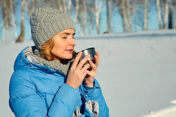 Mujer en un paseo por el bosque de invierno bebiendo té de un termo . — Foto de Stock