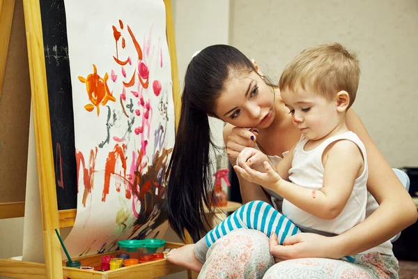 Little boy with mother paints a brush on an easel. painting child. — Stockfoto