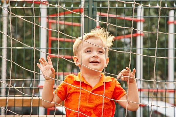 Funny little boy on playground with a grid of football gate. playing child on sports ground. — Stock Photo, Image