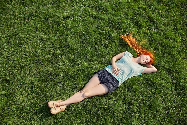 Nuori rentouttava punapää tyttö makaa nurmikolla. nainen rentoutuminen ulkona . — kuvapankkivalokuva