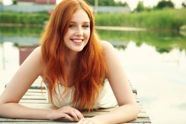 Kırsalda suyun arka planında genç kızıl saçlı bir kadının yaz portresi..