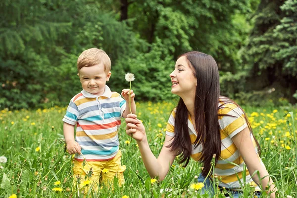 Ritratto esterno di una madre con suo figlio. Mamma e figlio camminano in un parco estivo sull'erba con denti di leone gialli . — Foto Stock