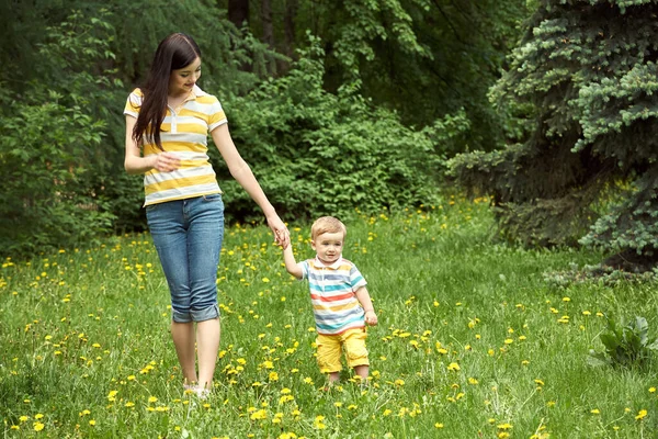 Outdoor portrait of a mother with her child. Mom and son walking in a summer park on the grass with yellow dandelions. — Stock Photo, Image