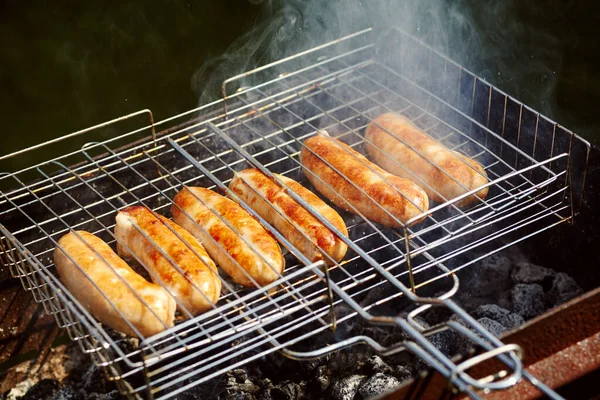 Le salsicce rubicund sono arrostite su carboni. Barbecue alla griglia nel fumo . — Foto Stock