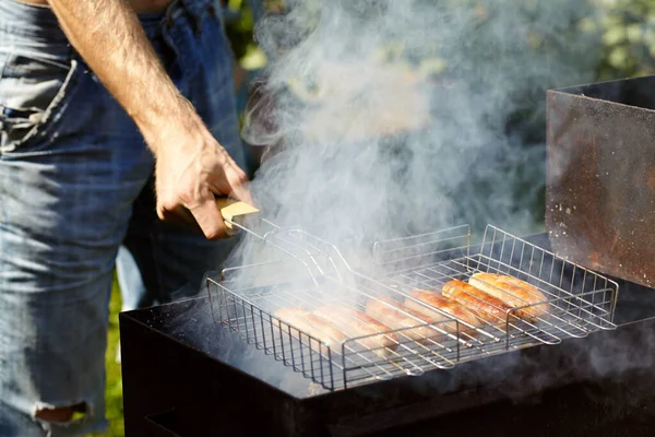 Le salsicce rubicund sono arrostite su carboni. Barbecue alla griglia nel fumo . — Foto Stock