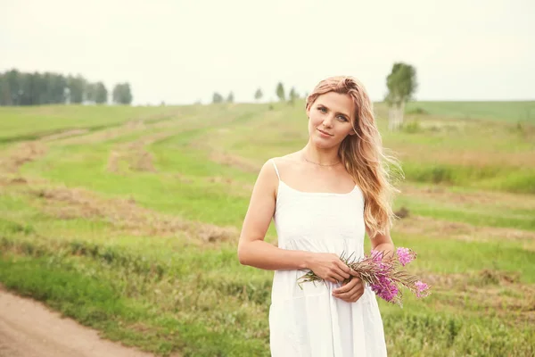Outdoor portret van een mooie blonde vrouw van middelbare leeftijd in een veld met bloemen. — Stockfoto