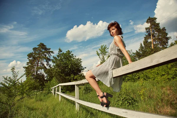 Verano relajarse retrato rústico de una joven sentada en la valla en el campo . —  Fotos de Stock