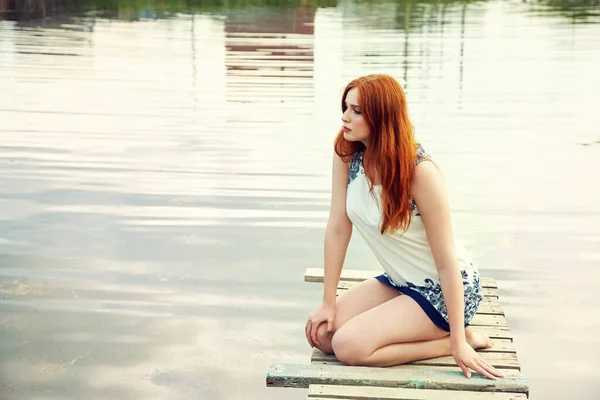 Retrato de verano de una joven pelirroja sobre el fondo del agua en el campo . —  Fotos de Stock
