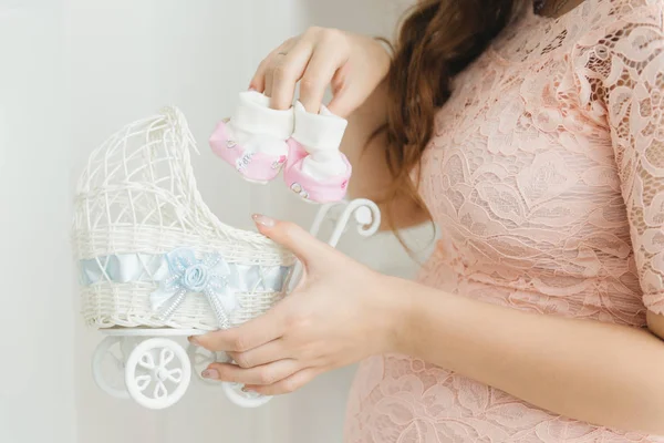 W ciąży dziewczyna gospodarstwa baby buciki i wózek — Zdjęcie stockowe