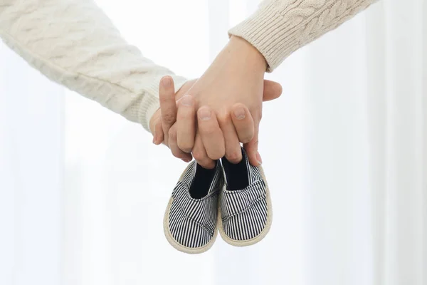 Les mains de papa et maman tiennent des chaussons pour bébé nouveau-né — Photo