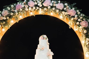 Şatafatlı dört katlı beyaz pasta, düğün kemerinde çiçekler.