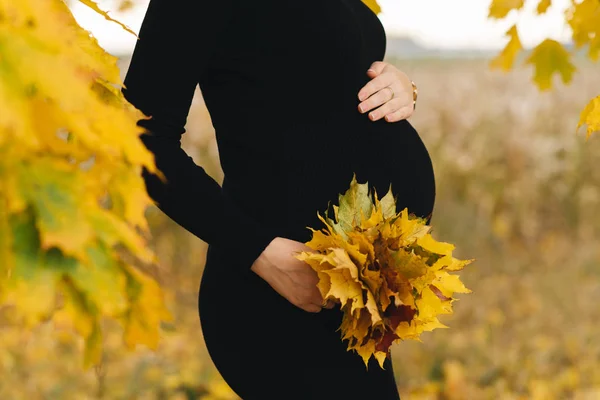 Ciężarna dziewczyna jesienią żółte liście blisko brzucha — Zdjęcie stockowe